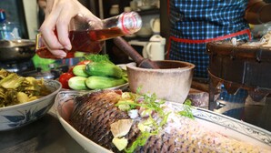 Un pescado grande siendo preparado con verduras y un cuenco de madera.