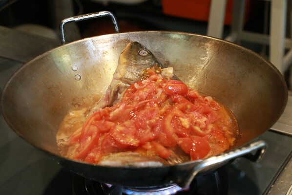 A wok with a fish and tomatoes on a stove. - Maison Haily (Hanoi)