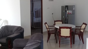 A living room with a sofa, a dining table with chairs, a refrigerator, and a door with a curtain. - Padmi Villa (Weligama)