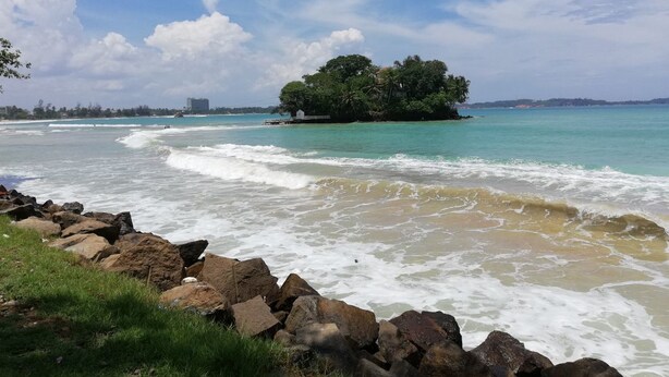 A beach with waves, a rocky shoreline, and a small island with trees. - Padmi Villa (Weligama)