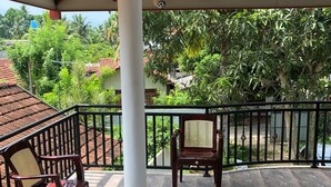 A covered balcony with a tiled floor, two wooden chairs, a decorative rug, and a view of greenery and buildings in the background. - Padmi Villa (Weligama)