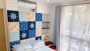 A bedroom with a bed, a headboard with nautical-themed panels, a window with curtains, and a built-in shelf unit.