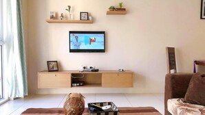 A living room with a television mounted on the wall, a wooden console table, a wicker elephant figurine, a checkered basket, and a patterned sofa.