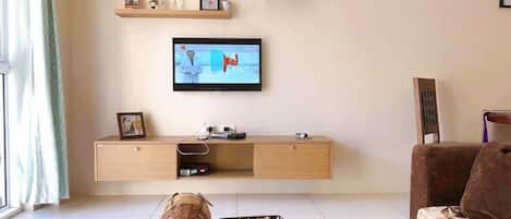 A living room with a television mounted on the wall, a wooden console table, a wicker elephant figurine, a checkered basket, and a patterned sofa.