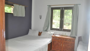 Ein Schlafzimmer mit einem Einzelbett, einem hölzernen Schminktisch, einem Fenster mit Vorhängen und einem kleinen Regal mit Gegenständen.