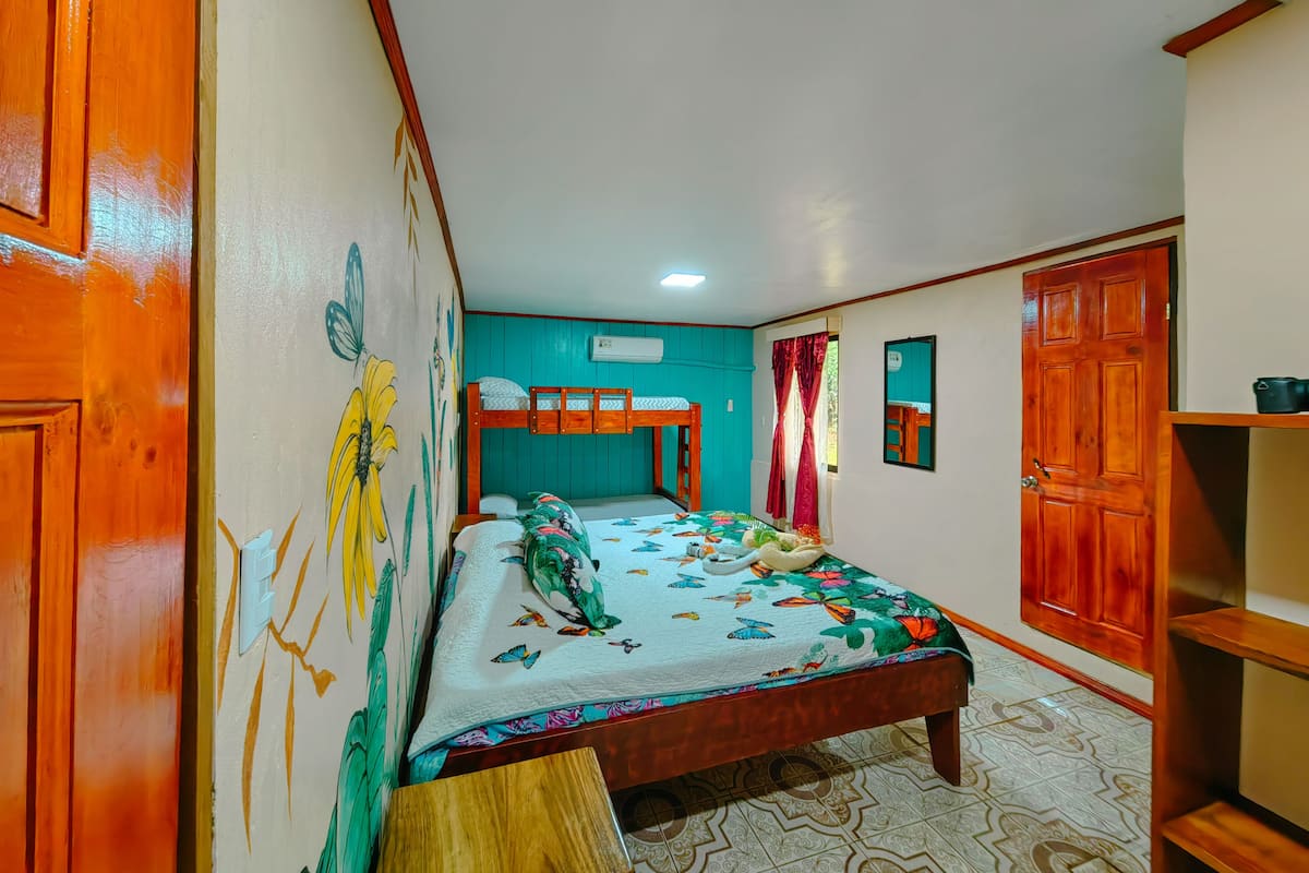 A room with a bunk bed, a single bed with a floral bedspread, a wooden bench, and a wall with a floral mural.