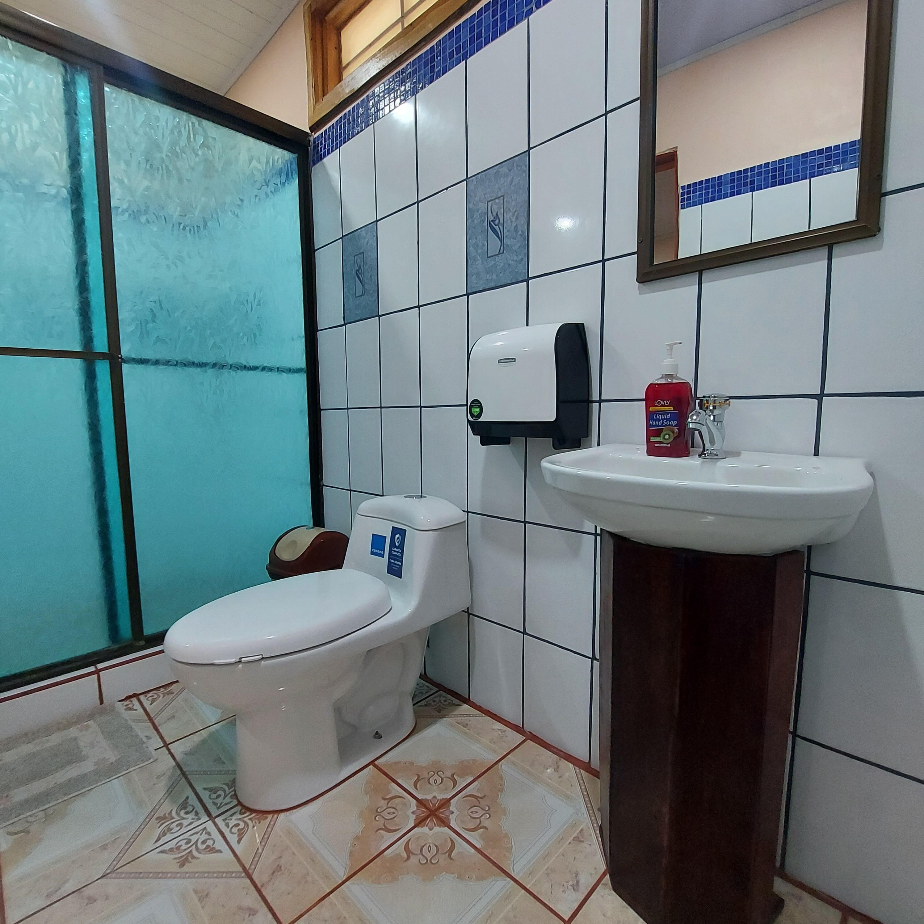 Un baño con inodoro, lavabo y dispensador de jabón para manos.