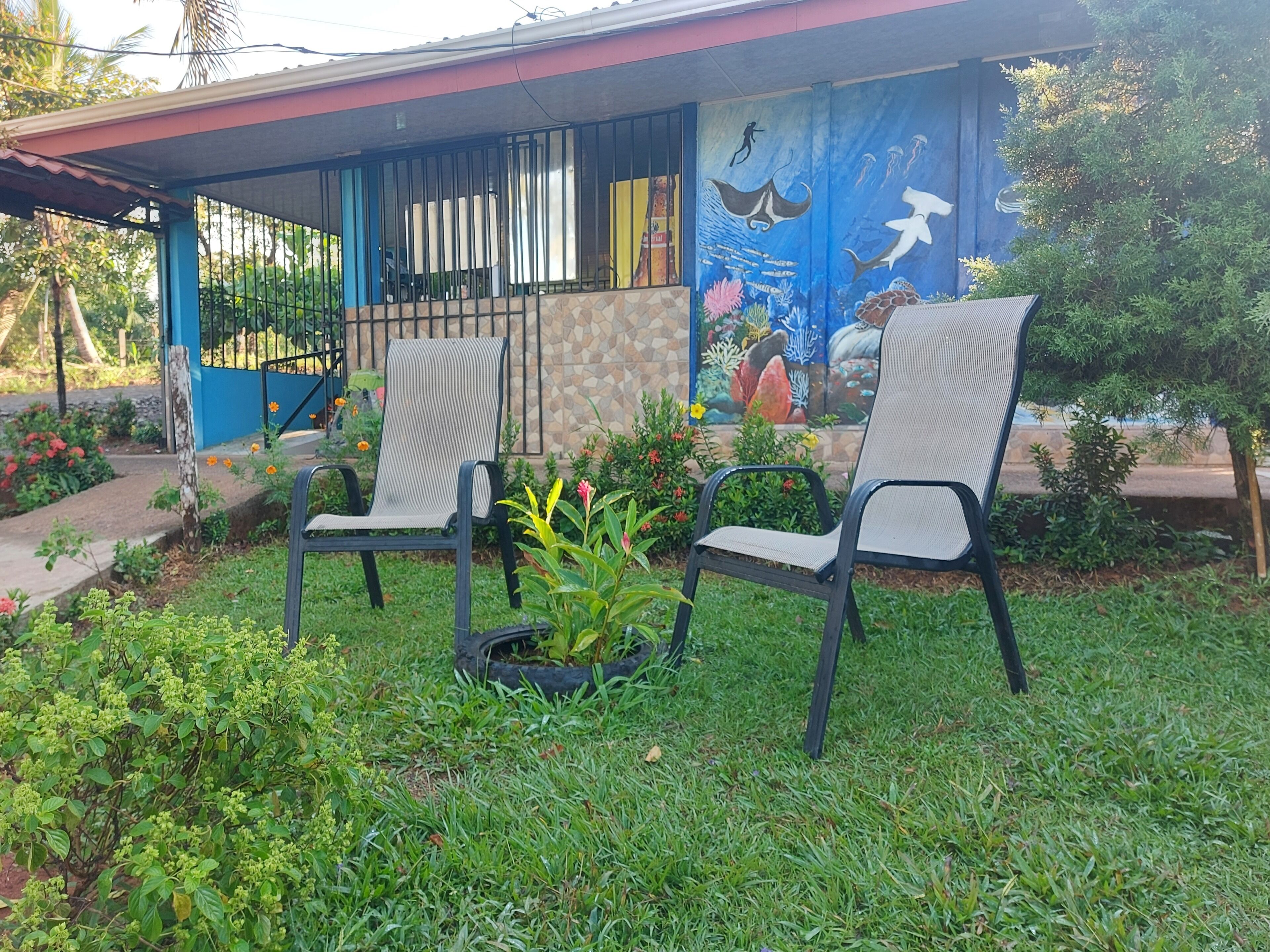 A covered outdoor seating area with two chairs and a small table, a mural with marine life, and a stone-tiled wall.