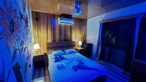 Une chambre à coucher avec une tête de lit en bois, un lit recouvert de draps blancs, une table de chevet avec une lampe et un climatiseur fixé au mur.