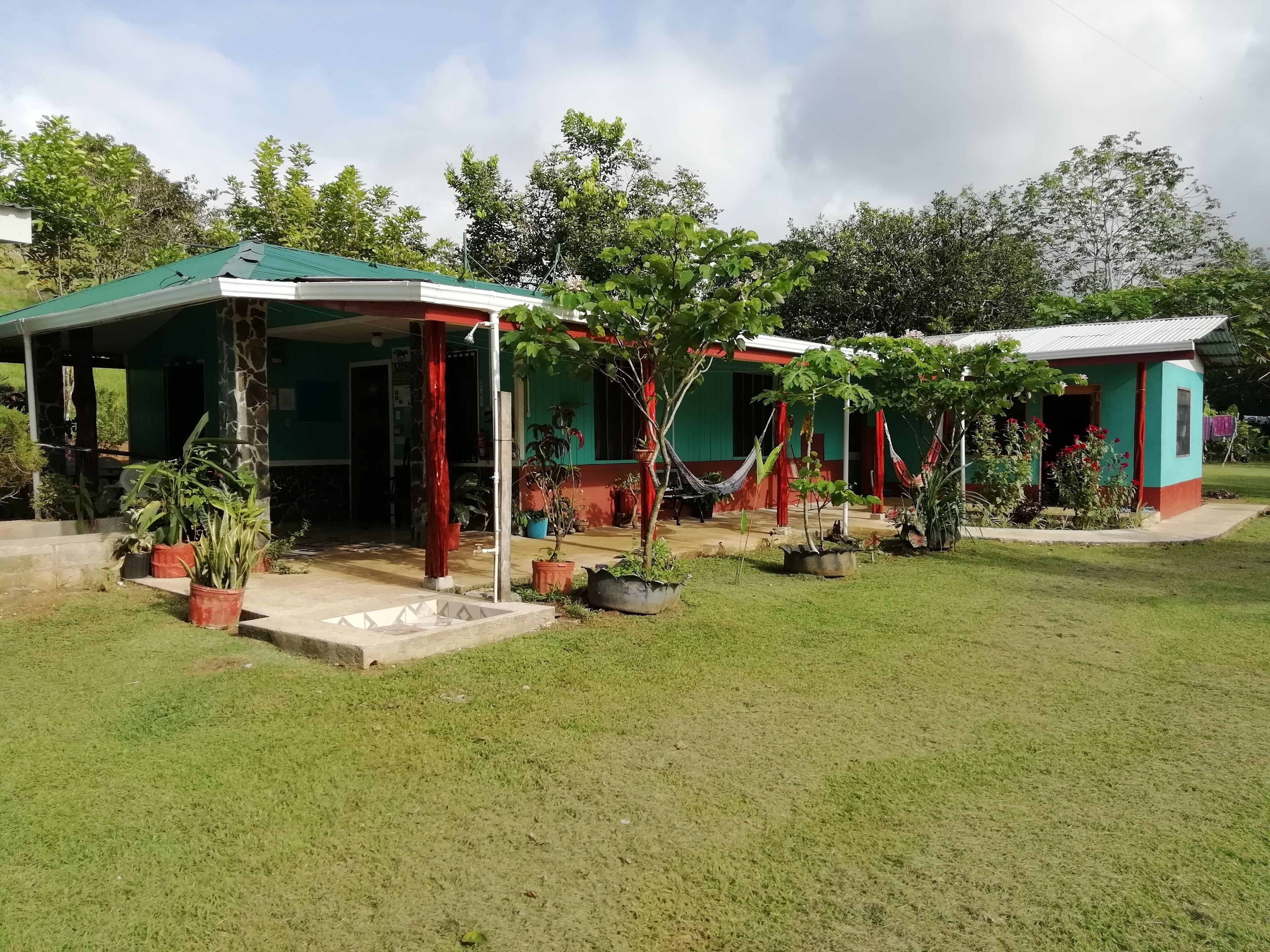 Uma casa com telhado verde, varanda e uma rede.