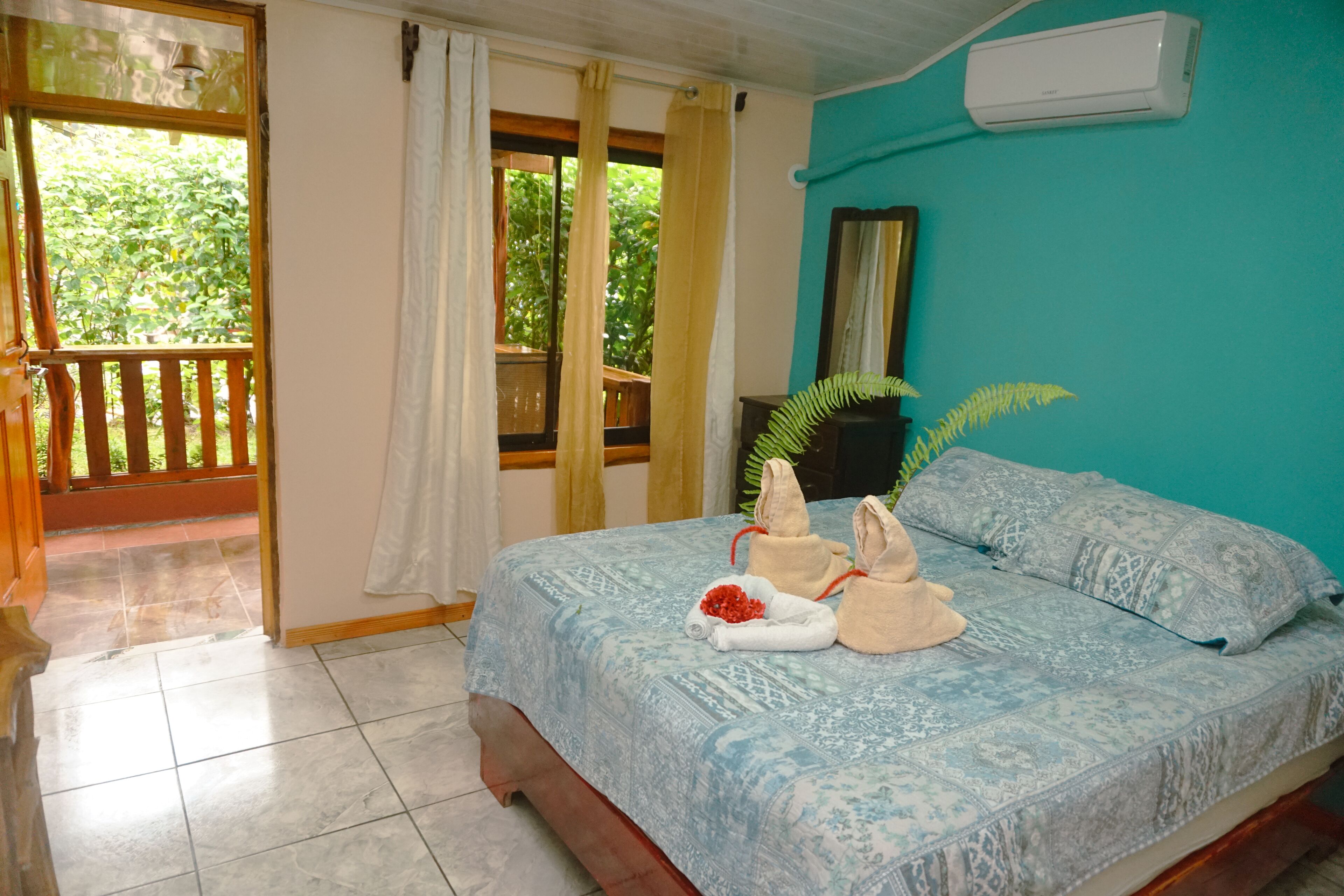 Une chambre à coucher avec un lit, une fenêtre avec des rideaux, une plante en pot et un appareil de climatisation.