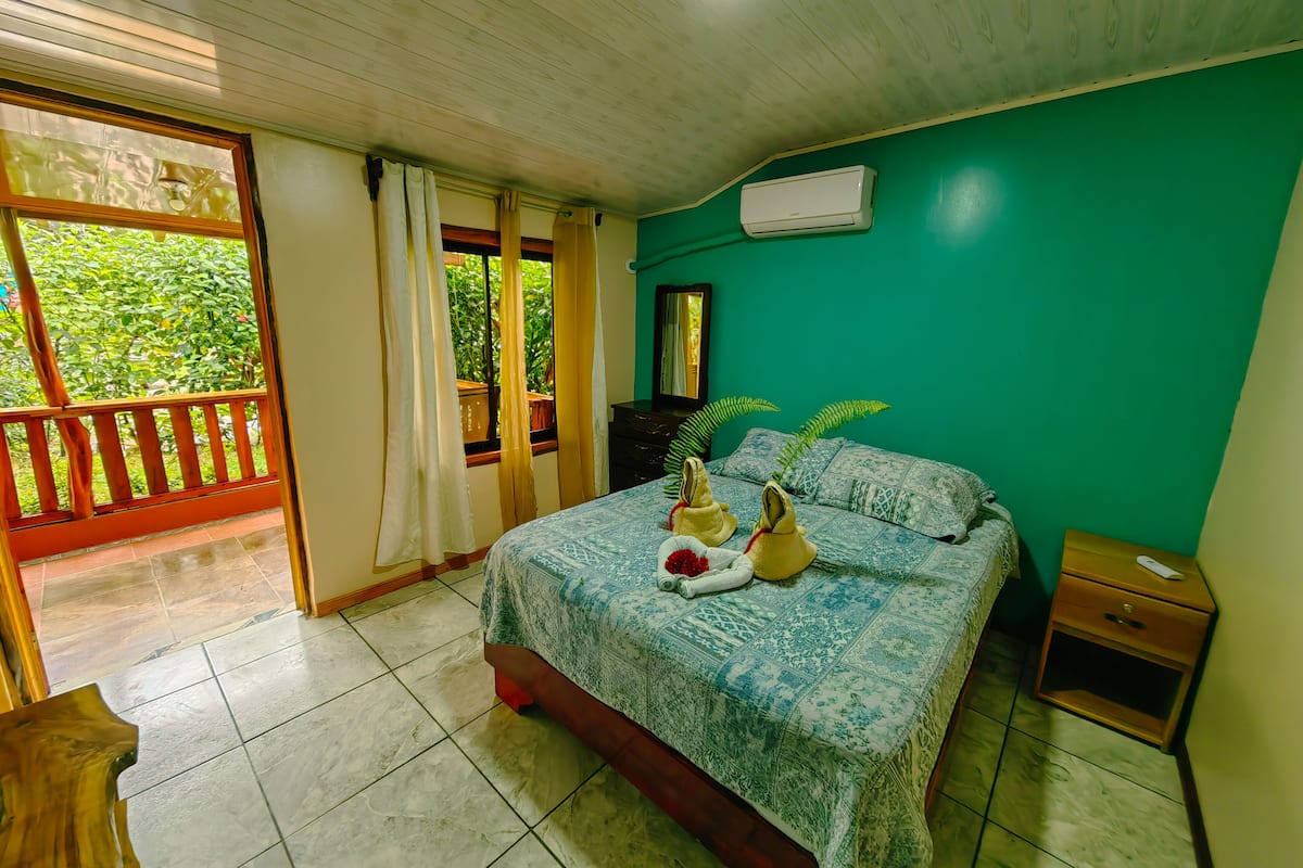 A bedroom with a bed, a nightstand, a mirror, and a window with curtains.