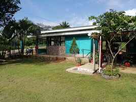 Una casa de una planta con techo blanco y paredes azul verdoso, rodeada de un césped cuidado y plantas en macetas.