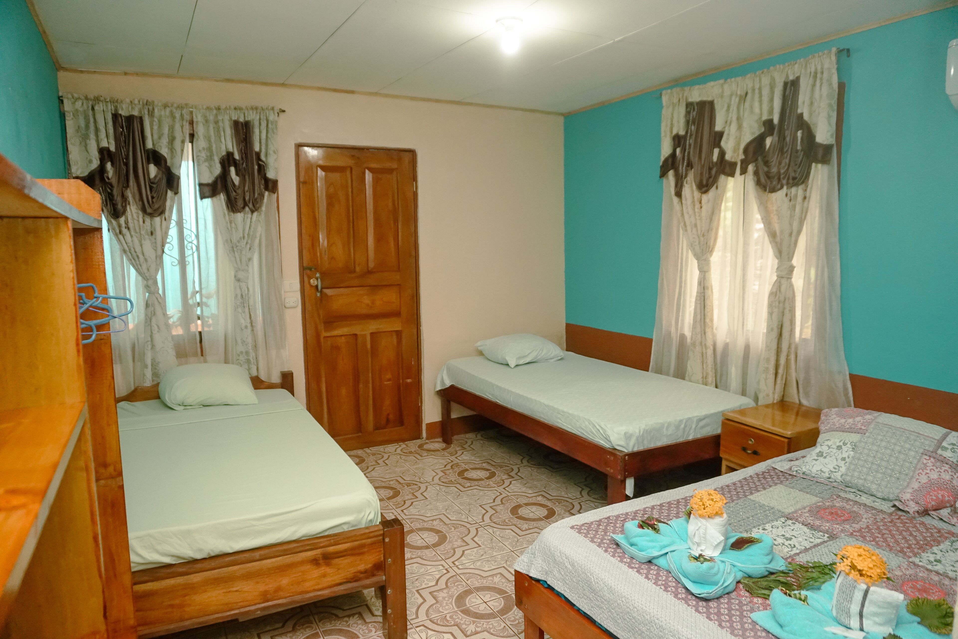 A room with two wooden beds, a wooden wardrobe, a wooden nightstand, and a patterned floor.