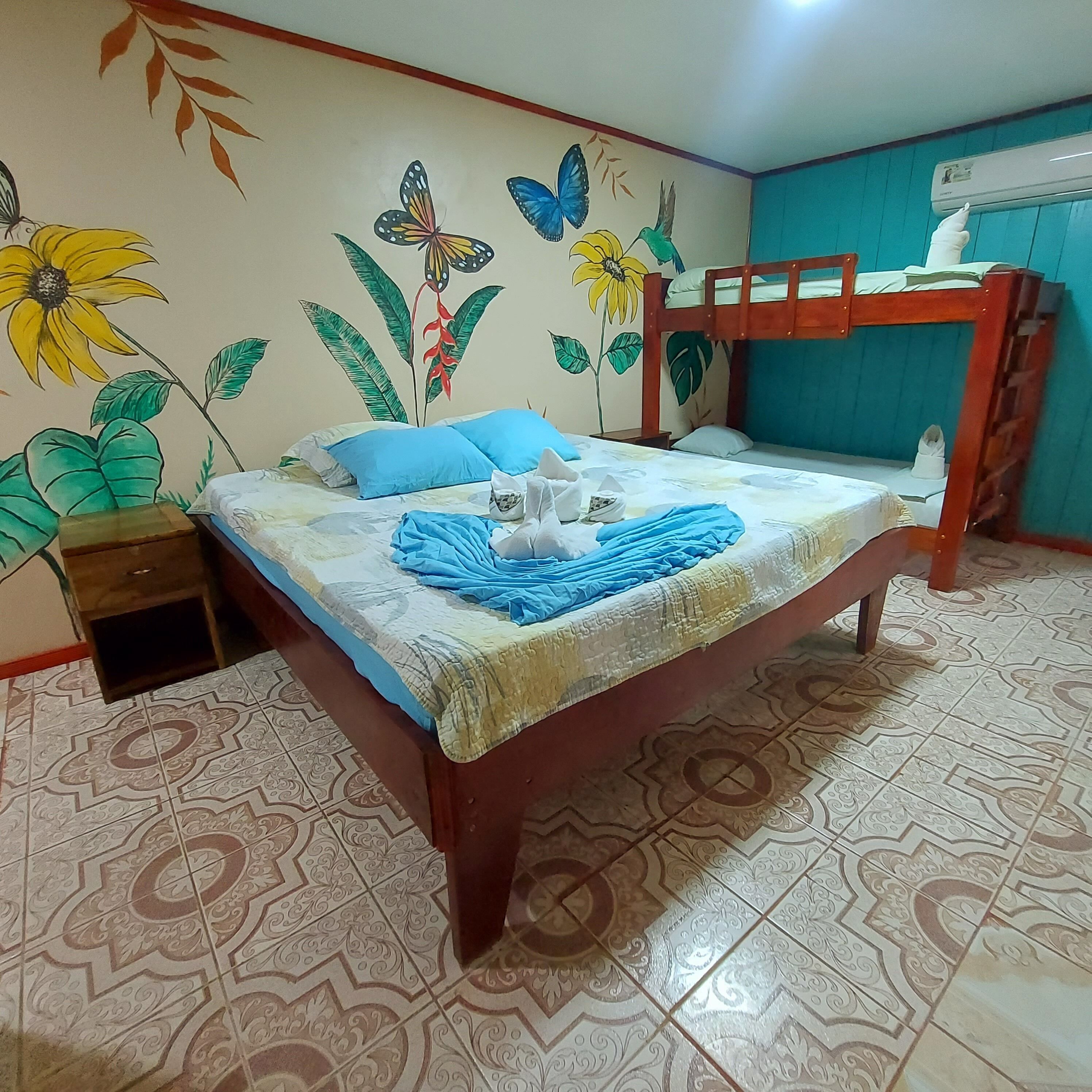 A bedroom with a bunk bed, a nightstand, a bed with blue and white bedding, and a wall mural with flowers and butterflies.