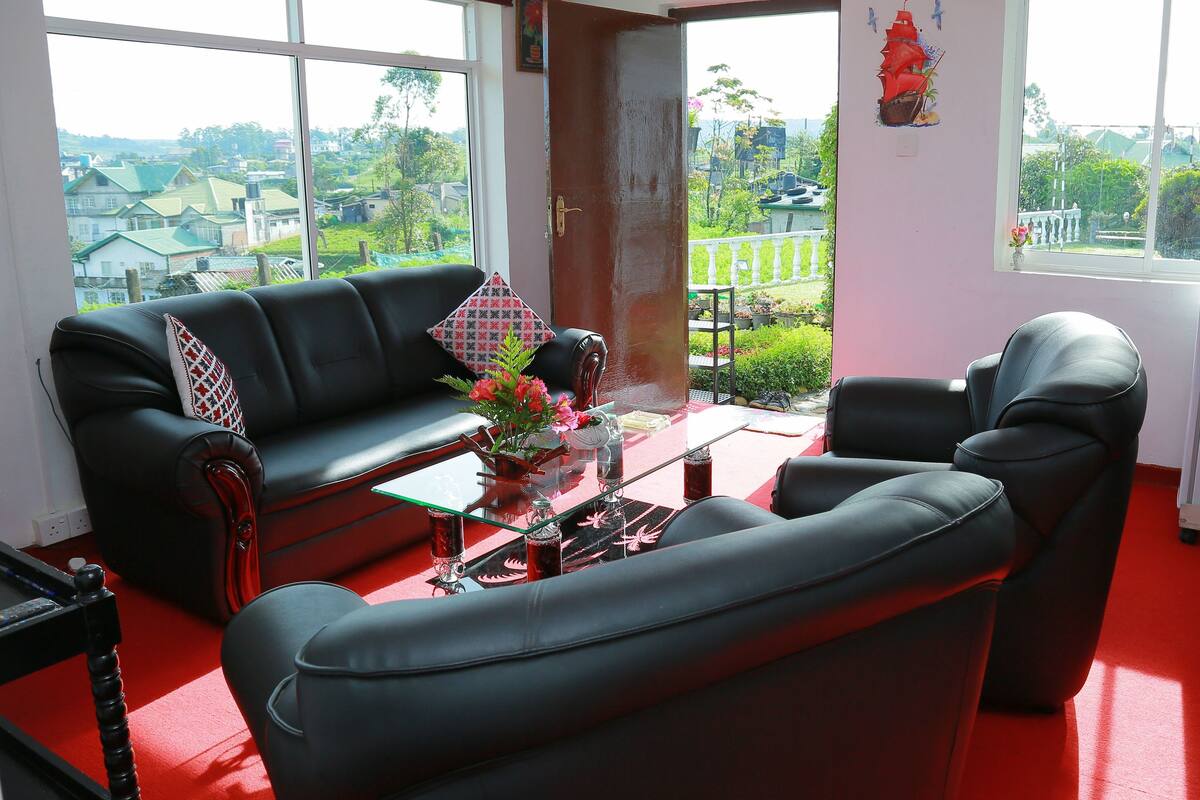 A living room with a black sofa, a glass coffee table, and a red carpet.