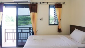 A hotel room with a bed, a window with curtains, an air conditioning unit, and a view of greenery outside.