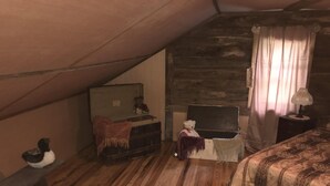 Een gezellig slaapkamer onder een schuine kap, met houten wanden, een bed met een beddeken met dessin, een klein tafeltje met een teddybeer, en een kledingkast met een deken.