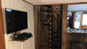 Een kamer met een wandtelevisie, een spiltrap en een bar met krukken.