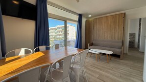 Ett modernt vardagsrum med ett matbord i trä, vita stolar, en grå soffa och en takfläkt.