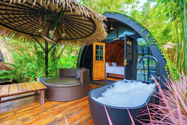 Un espacio exterior acogedor con un jacuzzi, muebles de madera y una estructura de techo de paja.
