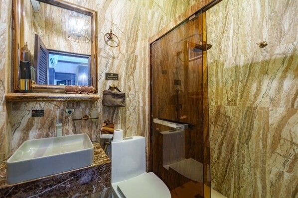 Un baño con paredes de mármol, un espejo grande, dos lavamanos, un inodoro y una ducha.