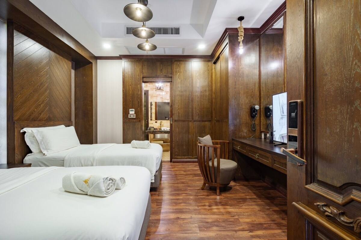 Une chambre d’hôtel avec deux lits, une armoire en bois, un bureau avec un téléphone et un miroir.
