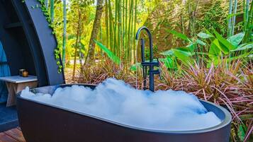 A large, dark-colored bathtub filled with ice, surrounded by lush greenery and bamboo plants.