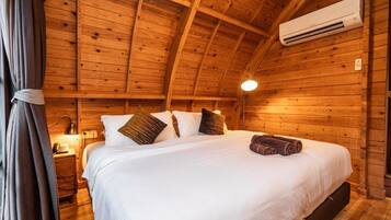 Un dormitorio de cabaña de madera con una cama, almohadas, una lámpara y un equipo de aire acondicionado.