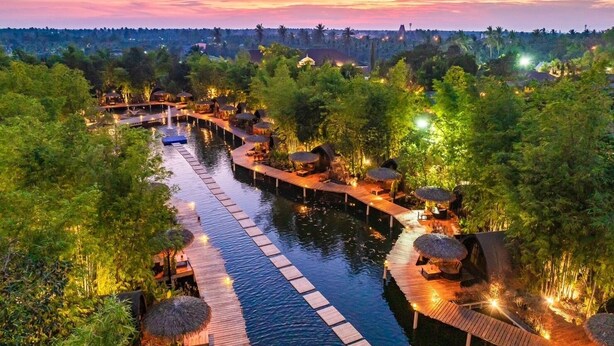 Ein Flussresort mit Holzstegen, strohgedeckten Hütten und einem ruhigen Gewässer.