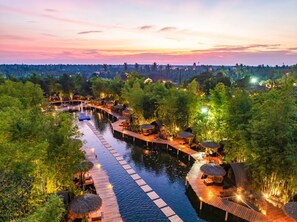 Ein Flussresort mit Holzstegen, strohgedeckten Hütten und einem ruhigen Gewässer.