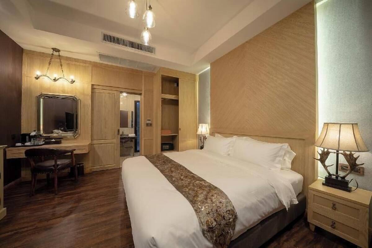 Une chambre d’hôtel avec un grand lit, un bureau avec une chaise, un miroir et une table de chevet avec une lampe.