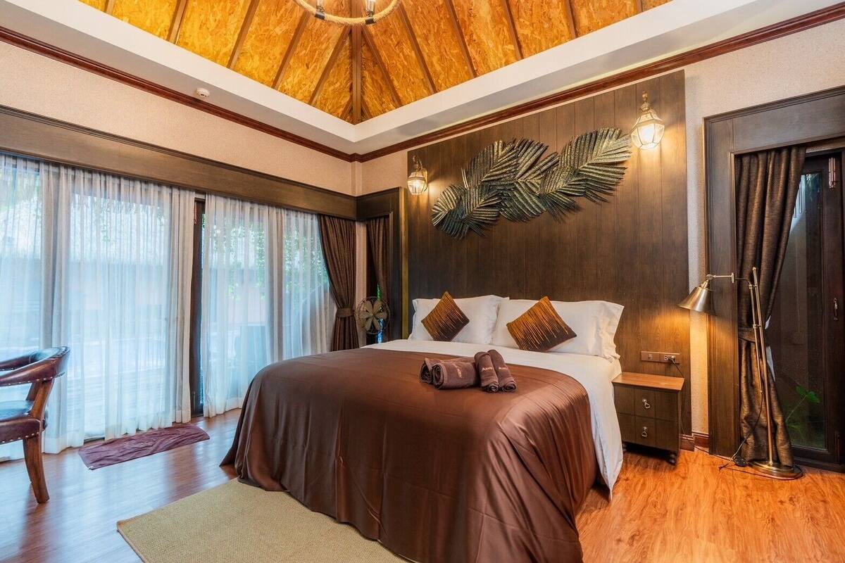 Une chambre avec un grand lit, un plancher en bois, un bureau et un plafond orné de panneaux en bois.
