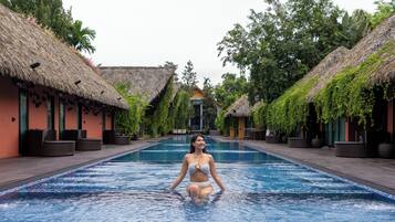 A pool area with thatched-roof buildings and lounge chairs.