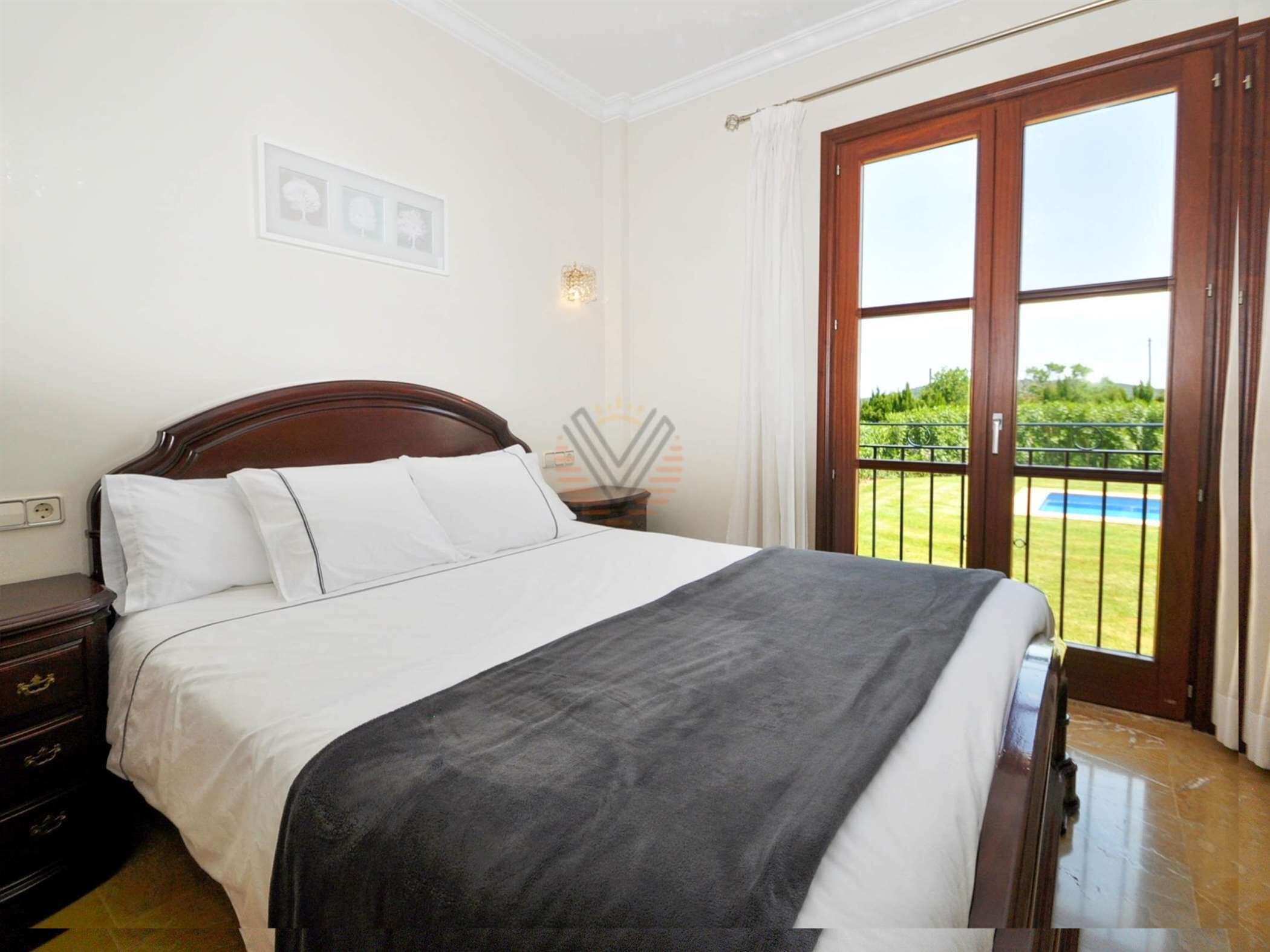 A bedroom with a large bed, a nightstand, a wall-mounted lamp, and a view of a pool through a sliding glass door.
