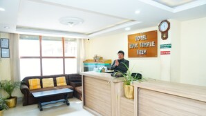 A hotel reception area with a wooden reception desk, a sofa, and a clock on the wall. - Hotel Holy Temple Tree & Chautari Cafe (Kathmandu)