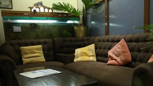 A brown sofa with yellow and pink cushions, a glass coffee table, and a potted plant. - Hotel Holy Temple Tree & Chautari Cafe (Kathmandu)