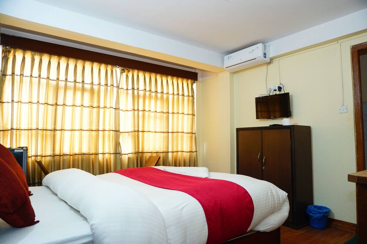 Quarto de hotel com cama, guarda-roupa, televisão na parede e ar condicionado.