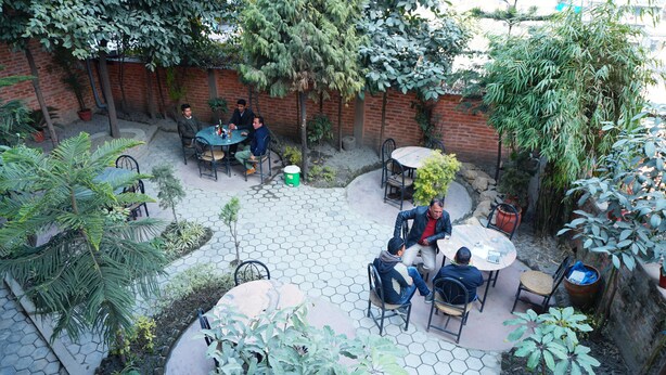 An outdoor patio area with hexagonal tile flooring, surrounded by potted plants and trees. - Hotel Holy Temple Tree & Chautari Cafe (Kathmandu)