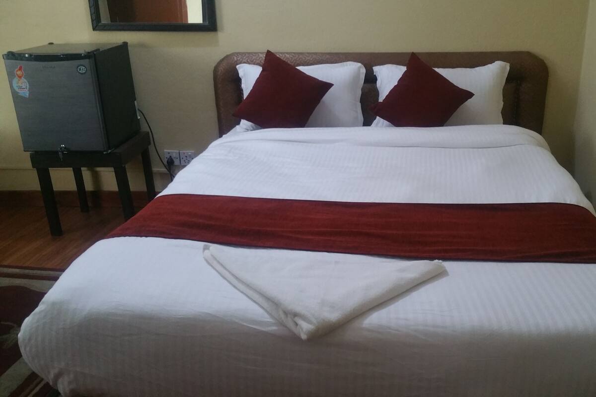 Uma cama bem arrumada com roupa de cama branca e vermelha, um cobertor vermelho e dois travesseiros.