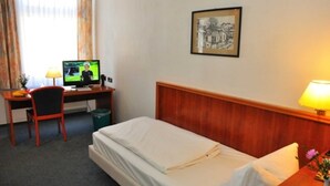 Una habitación de hotel con una cama individual, un escritorio con computadora, una silla y una lámpara.