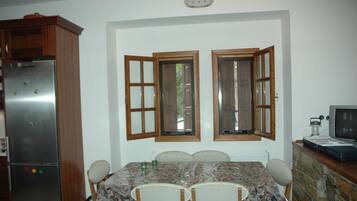A dining area with a table, chairs, a refrigerator, and a television.