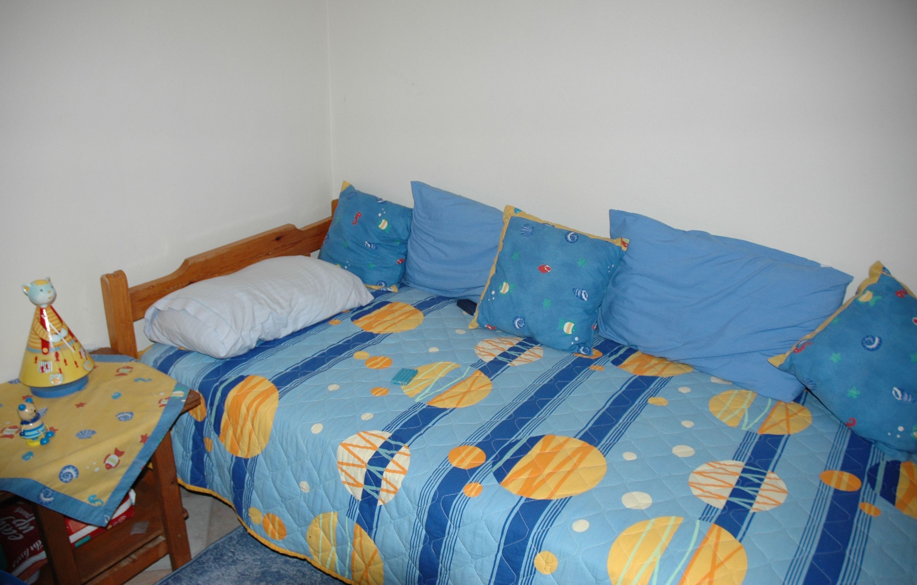 A bedroom with a bed, pillows, a table with a toy, and a chair.