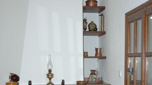 Ein Kamin aus Stein mit einem hölzernen Sims, ein Sessel und Regale mit Dekoration.