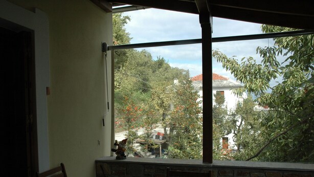 Ein Zimmer mit großem Fenster, das auf einen Garten und ein Gebäude blickt. Im Raum befinden sich ein Tisch und Stühle.