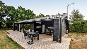 Un espacio al aire libre moderno con zona de comedor, terraza de madera, zona de estar cubierta y estación de barbacoa.