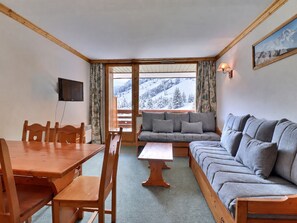 Una habitación con una mesa de comedor de madera, sillas, un sofá y un televisor colgado en la pared.