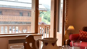A cozy room with a wooden table set for dining, a heart-shaped pitcher, and a view of a wooden building and greenery outside.