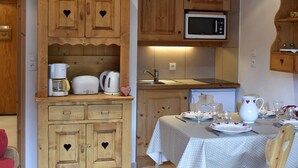 A compact kitchen with wooden cabinets, a microwave, and a dining area set for two with a table and chairs.