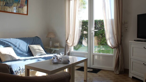 Ein Zimmer mit einem Bett, einem Tisch mit Gläsern und einem Fernseher, sowie einem Bild von Strandstühlen.